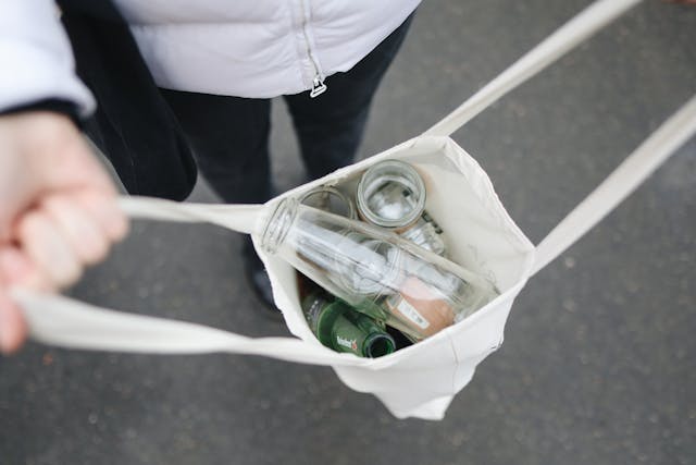 person holding open a white tote bag full of glass bottles